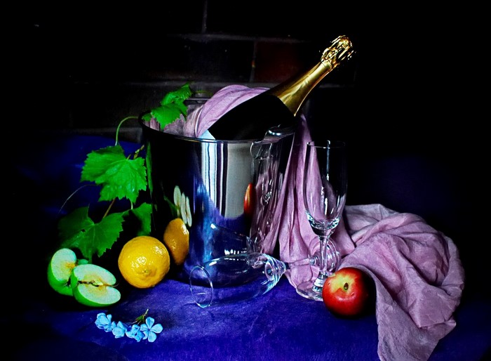 Champagne bottle in ice bucket with fruit and stemware