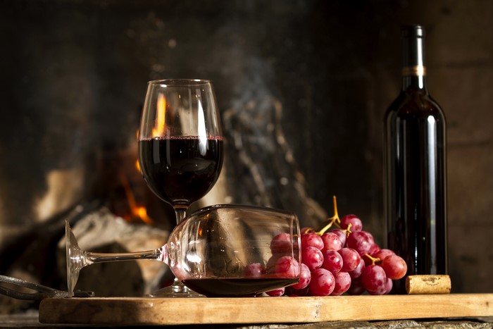 Still-life of wine, grapes, and bottle by fireplace
