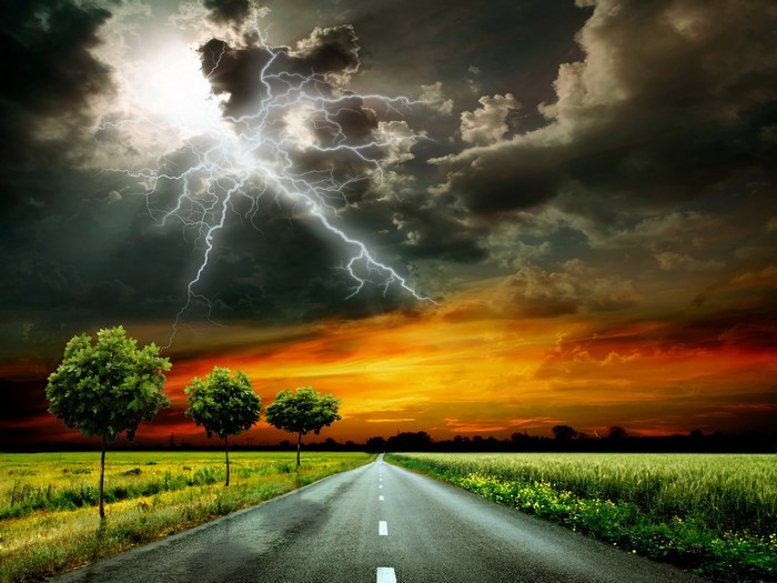 Road through fields under stormy sky with lightning