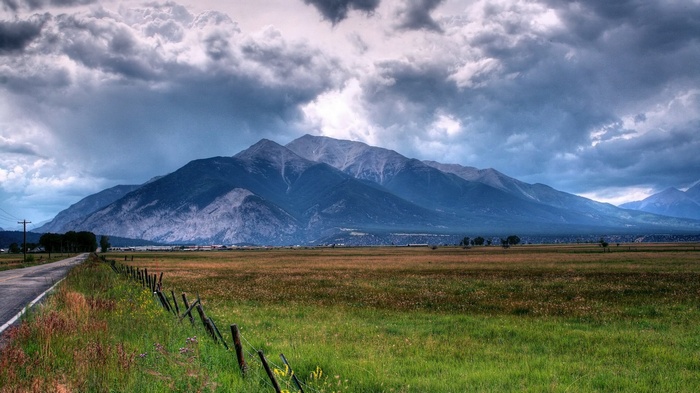 Mountain range under stormy clouds with a field and road