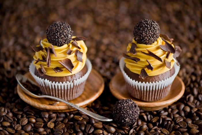 Two chocolate cupcakes with yellow frosting and chocolate shavings on coffee beans