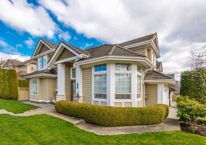 Tan house with bay window and manicured shrubs