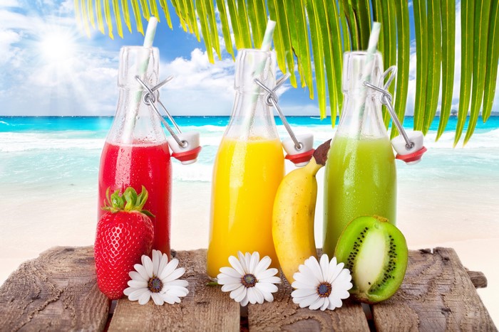 Strawberry, Banana, and Kiwi Juice Bottles on a Beach