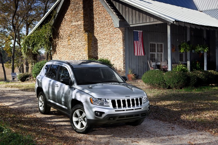 Silver Jeep Compass parked in front of a stone and wood house with American flag