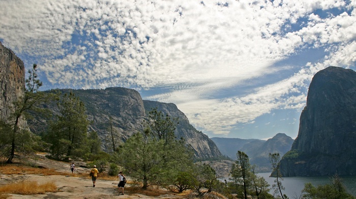 Hikers on a rocky trail with granite cliffs and a lake