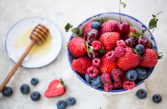 Bowl of fresh berries with honey dipper