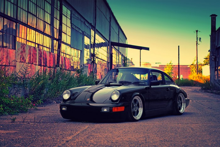 Black Porsche 911 parked in front of an abandoned building