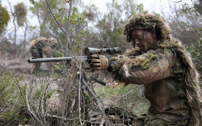 Soldier in ghillie suit aiming sniper rifle