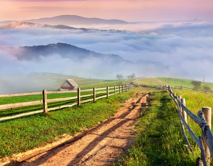 Dirt Road Through Misty Mountains with Wooden Fence