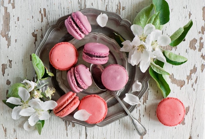 Pink and purple macarons on a silver platter with flowers