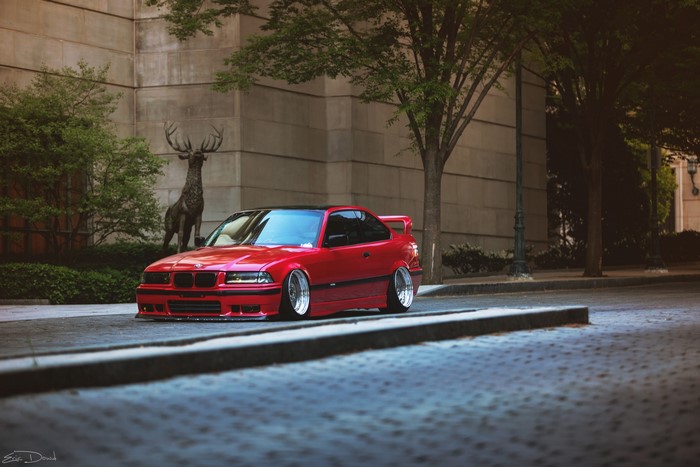 Red BMW E36 parked near a deer statue
