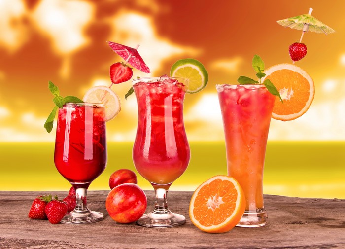 Three colorful cocktails with fruits and garnishes on a wooden table