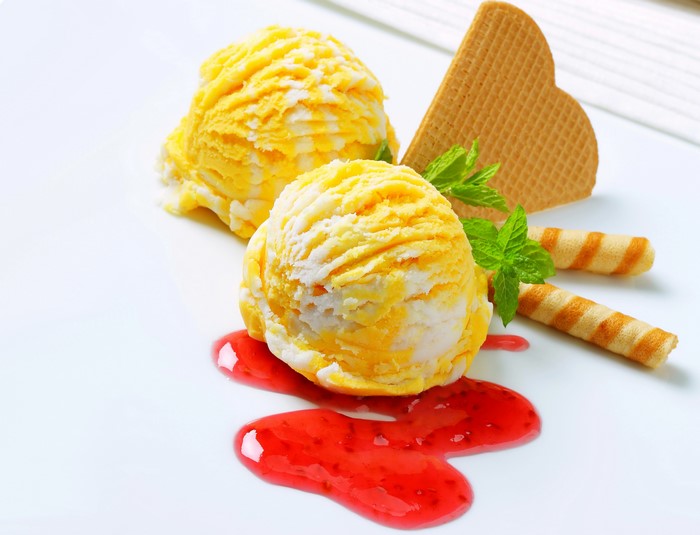 Two scoops of swirled yellow and white ice cream with strawberry sauce and wafers
