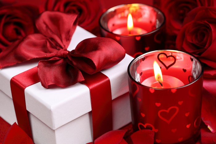 Gift box with red ribbon and candles near roses