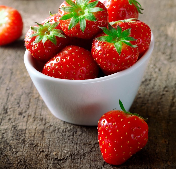 Strawberries in a white bowl on a wooden surface