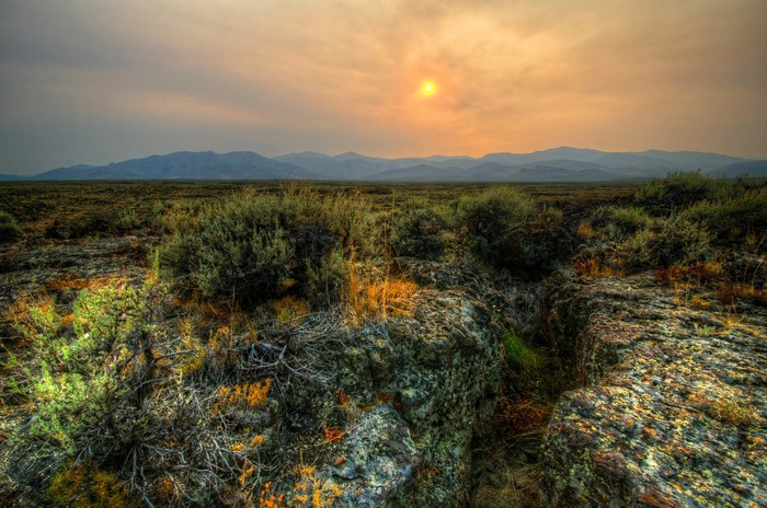 Sagebrush steppe with mountains under hazy sunset sky