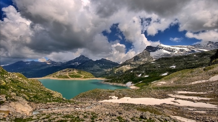 Turquoise lake surrounded by rocky mountains and dramatic clouds