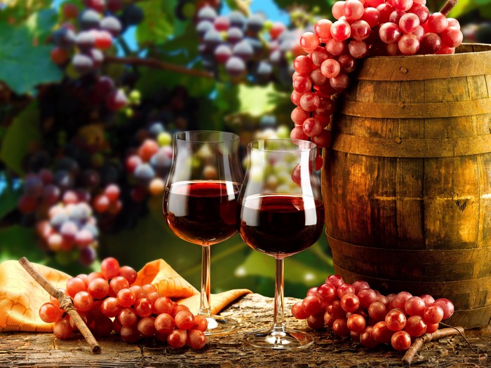 Red wine in glasses with grapes and barrel