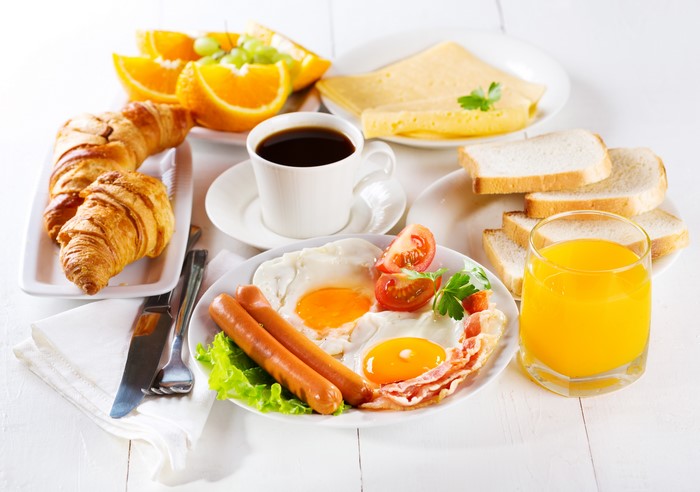 Breakfast with Croissants, Fried Eggs, Sausages, Coffee, and Orange Juice