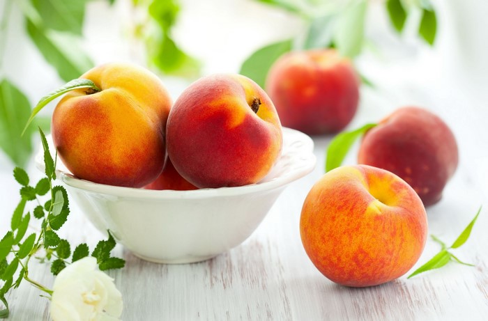 Peaches in a bowl with leaves and a rose