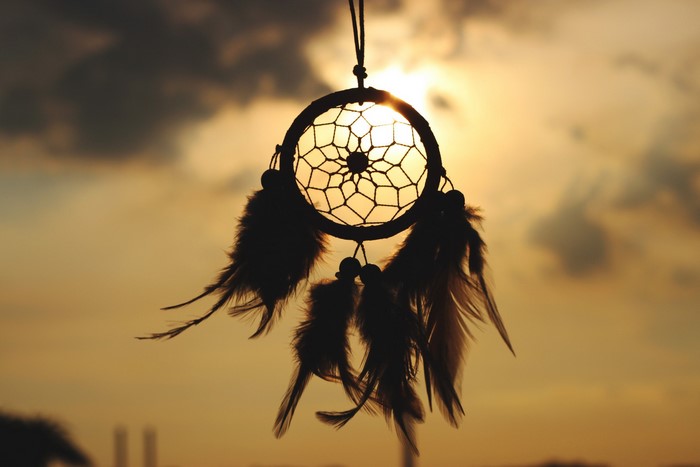 Silhouette of a dreamcatcher with feathers at sunset