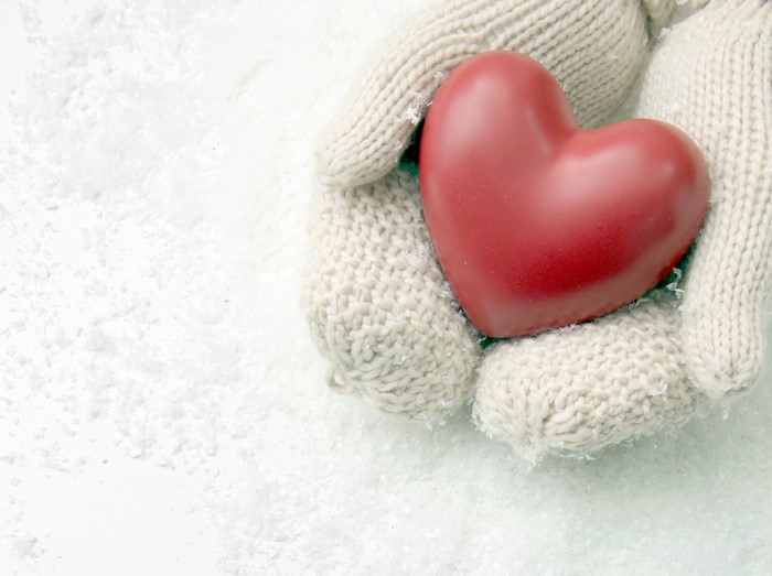 Hands in mittens holding a red heart in snow