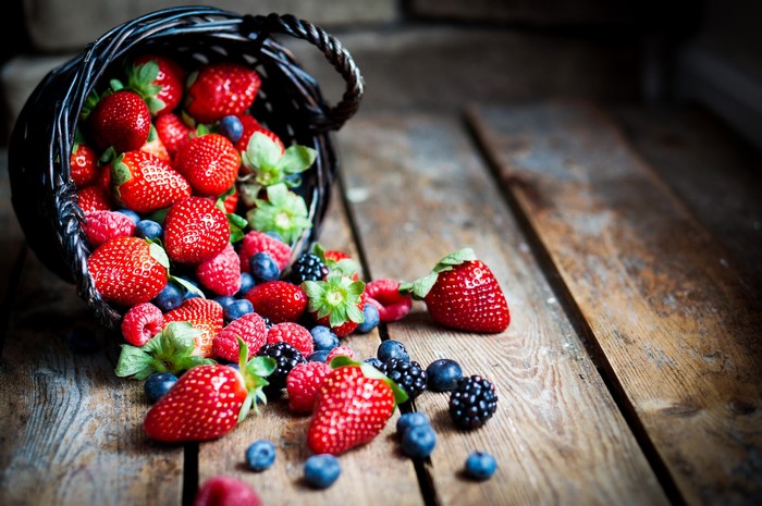 Berries spilling from a wicker basket onto a wooden surface