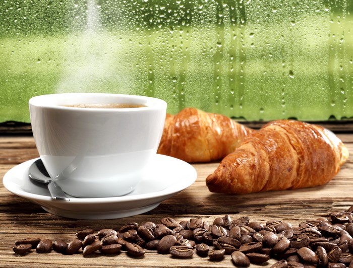 Coffee and croissants on a wooden table with a rainy window