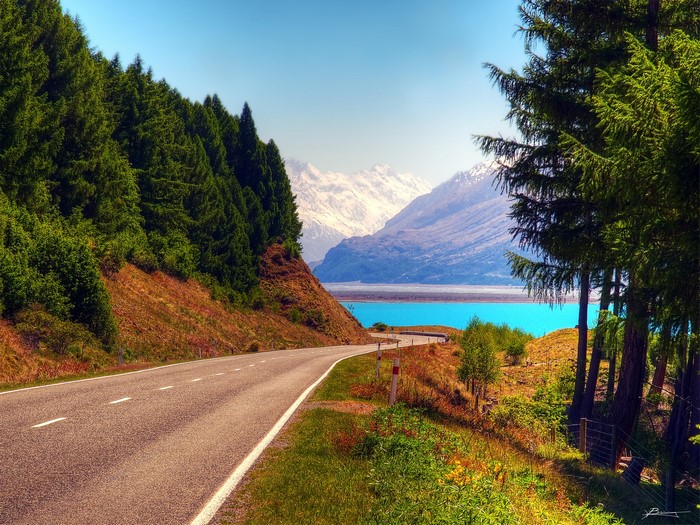 Road leading to a turquoise lake and snow-capped mountains