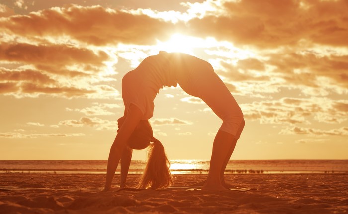 Woman doing a backbend on a beach at sunset