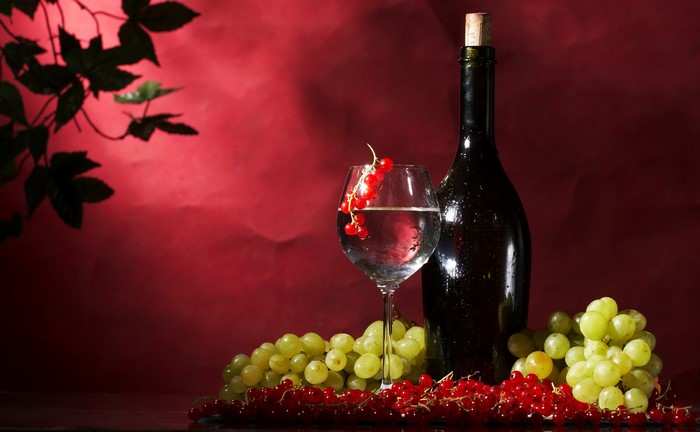 Wine bottle, glass, grapes, and currants on a red background