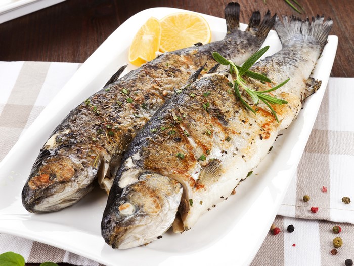 Two grilled fish with lemon and rosemary on a platter