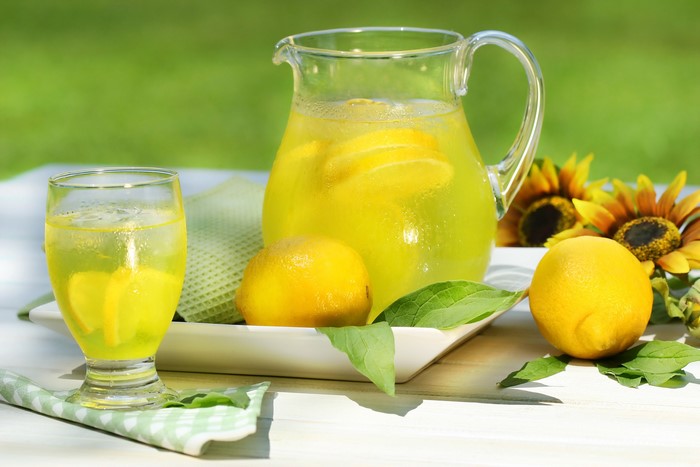 Pitcher and glass of lemonade with lemons and sunflowers