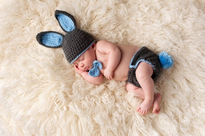 Baby in a crocheted bunny costume sleeping on a rug