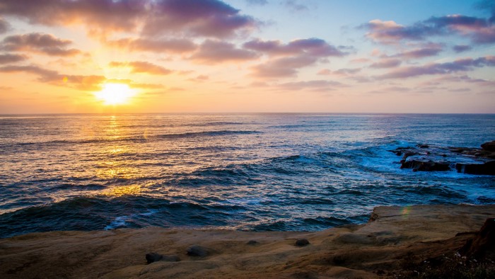 Sunset over the ocean with waves crashing on the coast
