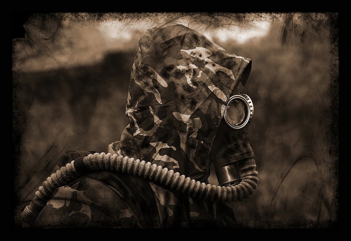 Man in camouflage hood and gas mask with hose