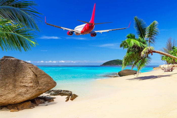 Airplane flying over a tropical beach with palm trees