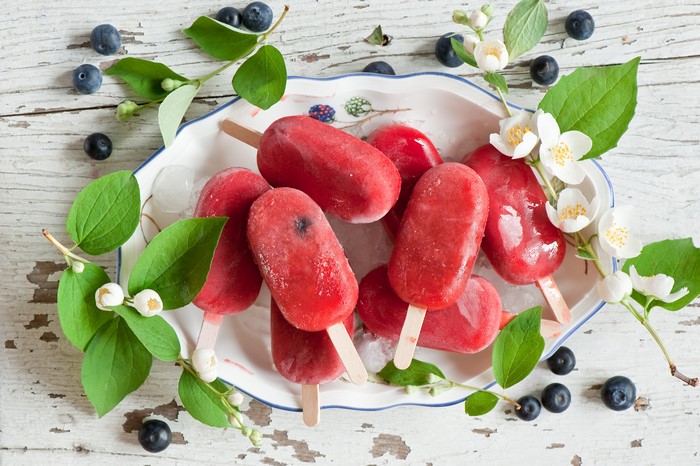Red popsicles with blueberries and jasmine on a plate