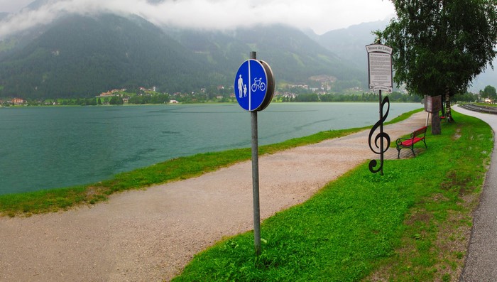 Path by a lake with mountains and a signpost