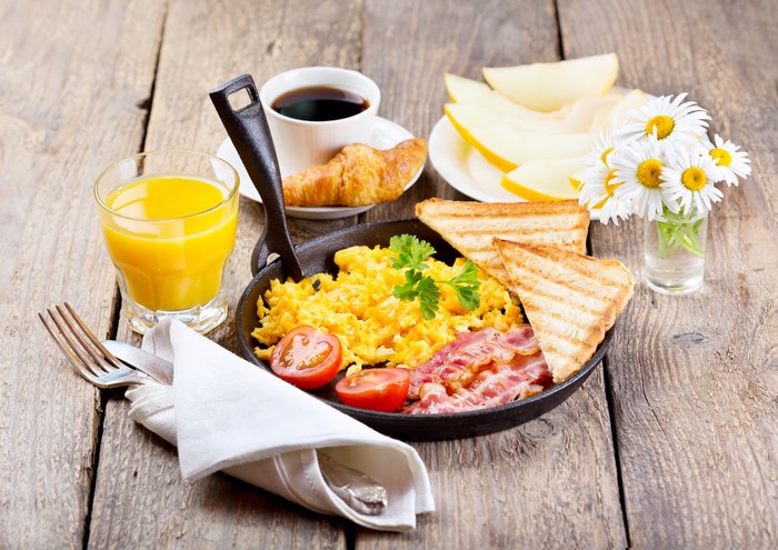 Breakfast with scrambled eggs, bacon, toast, juice, coffee, and fruit