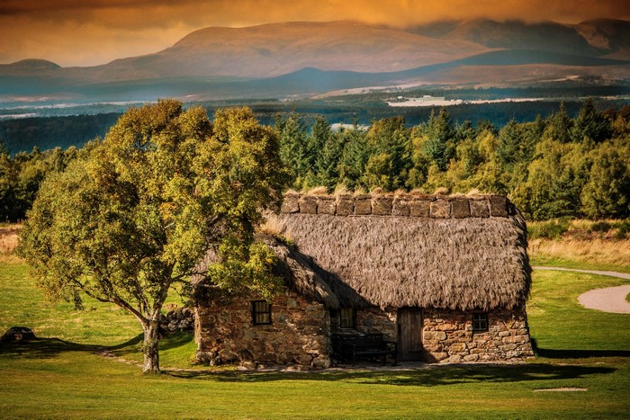 Thatched roof cottage in Scotland with mountains in background