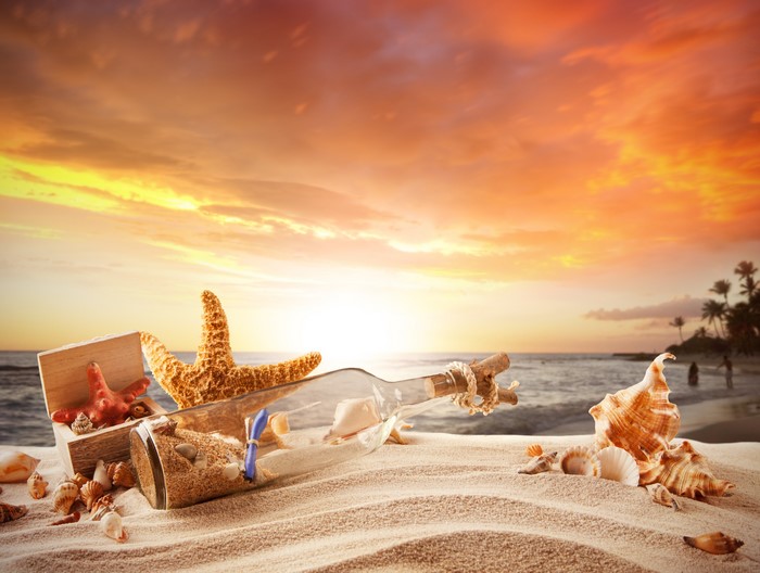 Message in a bottle with seashells on beach at sunset