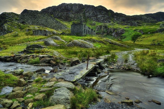 Stone bridge over stream in front of mountain ruins