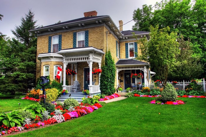 Yellow brick house with a Canadian flag and colorful flowers