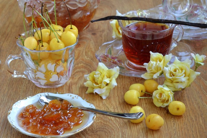 Yellow cherries, jam, tea, and roses on a wooden table