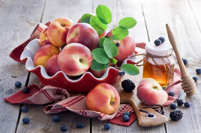Peaches, blueberries, blackberries, and honey jar on wooden table