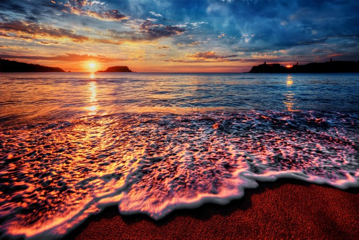 Sunset over the ocean with waves crashing on the shore
