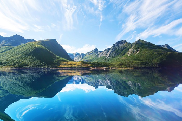 Mountains reflected in a calm lake under a blue sky with wispy clouds