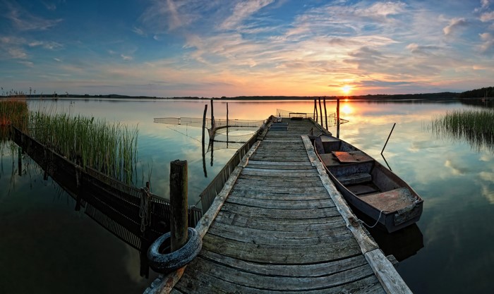 Wooden pier with boat at sunset over lake