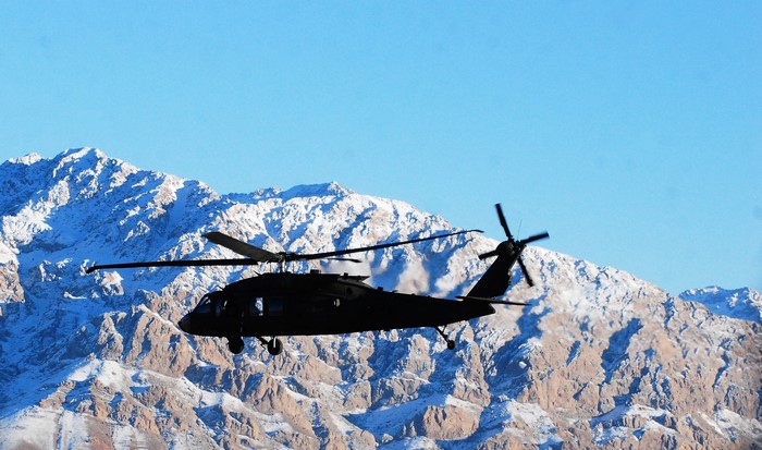 UH-60 Black Hawk helicopter flying over snow-covered mountains